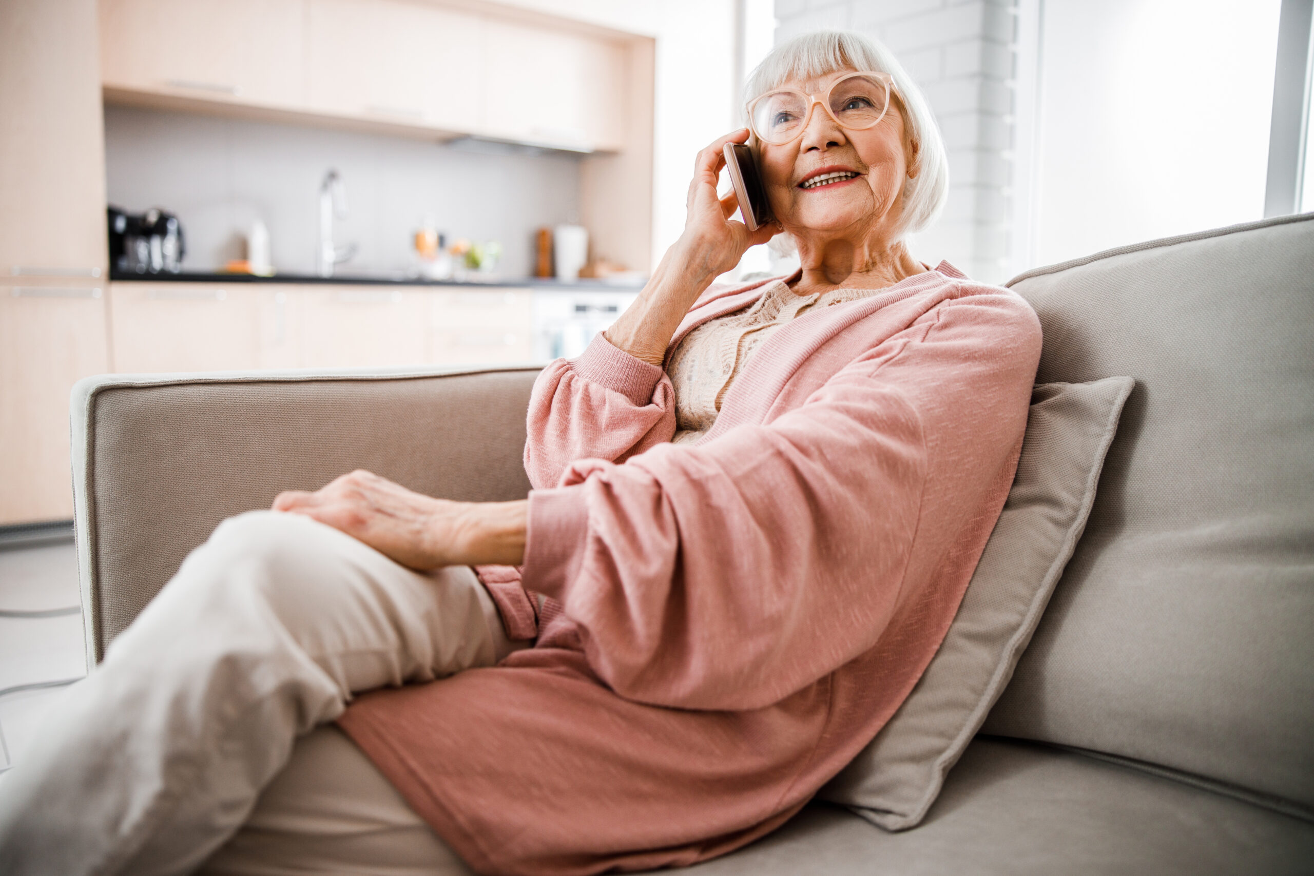 Cheerful senior woman sitting on couch and having phone conversation stock photo